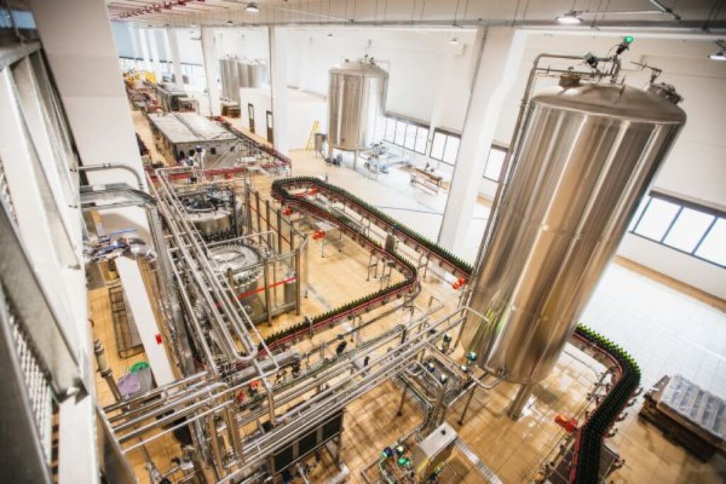 Vista superior de uma fábrica de bebidas com tanques de aço inoxidável e linha de envase automatizada de garrafas.