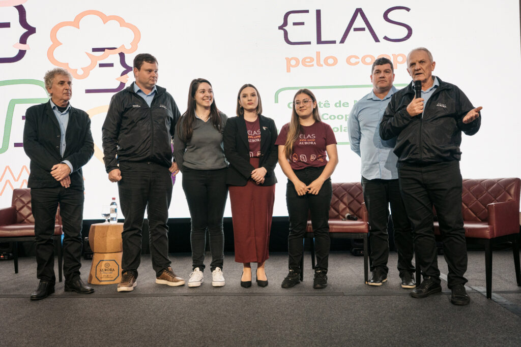 Sete pessoas estão em pé no palco durante um evento da Vinícola Aurora.