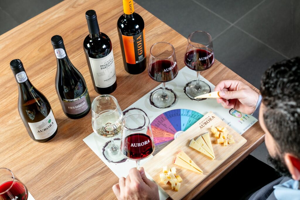 Pessoa participa de degustação de vinhos e queijos da Vinícola Aurora em mesa de madeira.