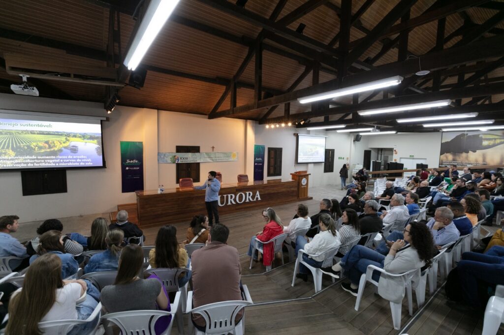 Palestrante apresenta sobre manejo sustentável para um auditório cheio de participantes na sede da Cooperativa Vinícola Aurora.