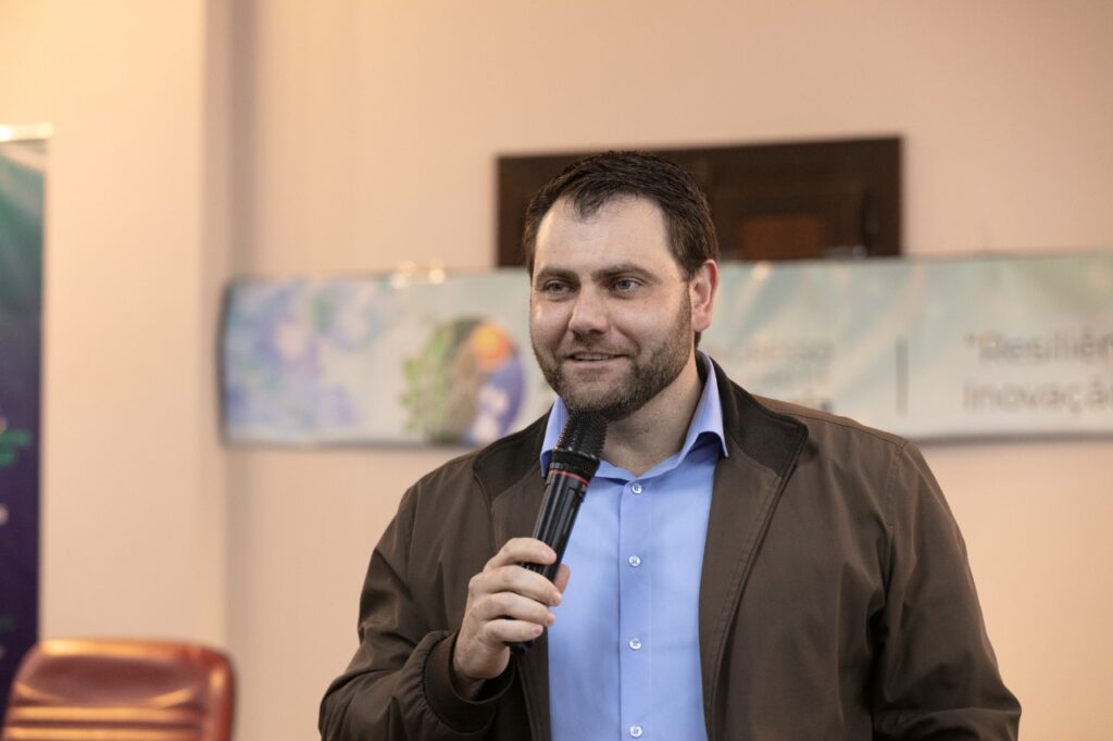 Homem falando ao microfone durante evento na Cooperativa Vinícola Aurora.