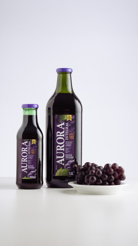 Garrafas de suco de uva Aurora com cacho de uvas ao lado.