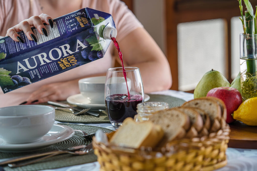 Pessoa servindo suco de uva Aurora em copo durante refeição.